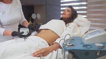 Esthetician employs spatula or applies cream to patient's abdomen in preparation for hair removal process. patient, young woman, is reclining on couch. video