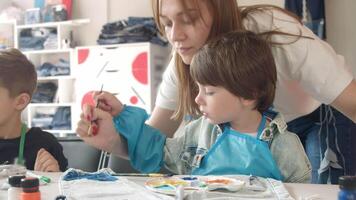 A caring young art teacher assists a boy in creating drawings on clothing during a master class. video