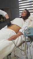 Before starting procedure, cosmetologist applies special gel to client's abdomen. This is done in order to prepare skin for use of device that will help remove excess weight and combat cellulite. video