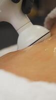 Cosmetologist performs procedure of ultrasonic anti-cellulite massage using figure-correcting device, massaging client's abdomen. video