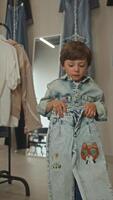 Child is delighted with his handiwork - one-of-a-kind jeans with distinctive style. He proudly shows them in clothing shop. Vertical. Portrait. video