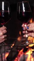 Two women clink glasses with each other with a glass of wine against the background of the fire in the fireplace. Warmth and home comfort, vertical footage video