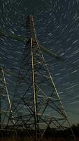 Witness the mesmerizing movement of stars illuminating the night sky above tall power lines in a serene rural landscape, vertical footage video
