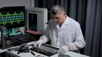 A focused technician in a lab coat meticulously fixes a circuit board on a table. Monitors display electronic signals, highlighting a high-tech environment. video