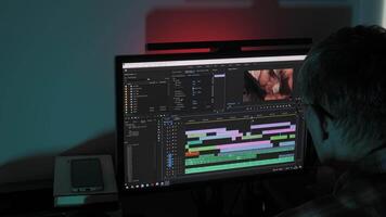 Man editing colorful timeline on a widescreen monitor in dark room, Focused editor works on post-production project at night using professional software interface video