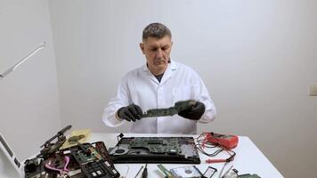 Engineer Examining Laptop Motherboard at Workbench, Technician in lab coat analyzing computer motherboard on desk with tools and disassembled hardware video