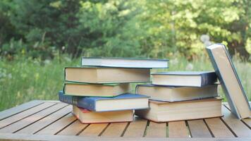 Stack of Hardcover Books on Wooden Table Outdoors, Educational literature arranged in nature setting during sunny summer day in forest meadow video