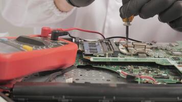 Technician Repairing Motherboard with Tools and Multimeter, Close-up of hands fixing circuit board using screwdriver and diagnostic device in lab coat video
