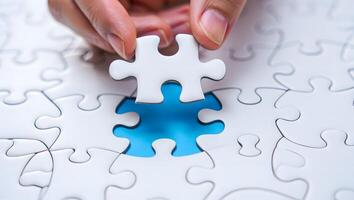 Hand placing the final white puzzle piece into a blue gap completing the picture photo