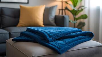 Cozy blue quilted throw blanket folded on a light gray ottoman in a modern living room photo