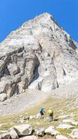 Two intrepid hikers embark on a challenging ascent up a majestic, rugged mountain under a clear blue sky, embracing the vast wilderness adventure. photo