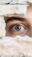A compelling close-up of a human eye, filled with curiosity, peeking through a narrow gap in an old stone wall, hinting at hidden observation. photo