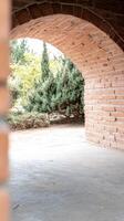 Sunlit brick archway framing a lush garden vista, inviting passage through ancient masonry into a tranquil natural outdoor space with vibrant green foliage. photo