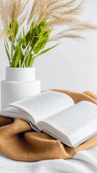 Serene Reading Nook Open Book on a Warm Blanket, Complemented by Elegant Pampas Grass in a White Vase, Evoking Comfort and Calm. photo