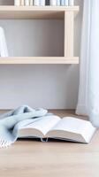 A serene and inviting scene of an open book and a soft blanket on a light wooden table, creating a perfect atmosphere for quiet reading and relaxation at home. photo