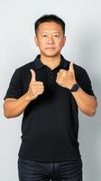 Mature Asian Man in Black Polo Shirt Giving Double Thumbs Up, Exuding Confidence and Approval Against a Clean White Background. photo