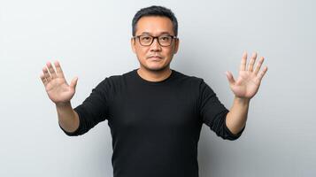 Mature Asian man in glasses raising both hands in a clear stop gesture, conveying a direct message of refusal or boundary against a minimalist studio background photo
