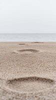 Sublime Footprints Etched in Golden Sand, Stretching Towards the Vast, Calm Ocean and Distant Horizon Under a Serene, Overcast Sky. photo
