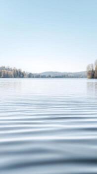 A tranquil lake scene with gentle ripples dancing across the water's surface under a clear, expansive sky, evoking profound serenity. photo