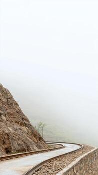 Journey into the Mist A Winding Mountain Railway Track Ascends Through Ethereal Fog, Revealing a Serene and Rugged Landscape Vista. photo