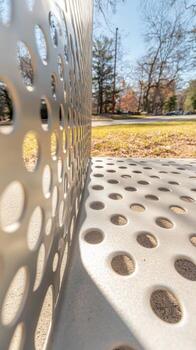 Captivating close-up of a modern perforated metal bench, showcasing intricate patterns of light and shadow in an outdoor park setting, a study in contemporary design. photo
