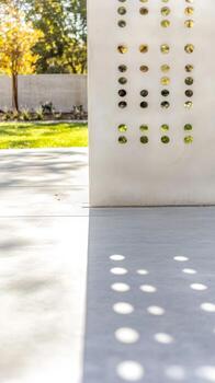 Modern Concrete Wall with Perforated Design, Capturing Playful Sunlight and Shadows on a Garden Pathway, Architectural Detail and Outdoor Serenity. photo