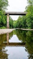 Concrete Bridge Spanning Tranquil River with Lush Green Forest Reflections photo