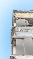 Striking Low-Angle View of a Severely Damaged Building Against a Clear Blue Sky, Highlighting Urban Decay and Structural Vulnerability. photo