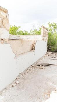 A poignant close-up of a crumbling concrete and stone wall, revealing layers of decay and the passage of time, set against a serene sky and lush green foliage. photo