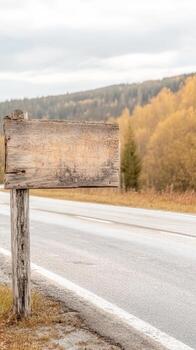 Aged wooden signpost by a tranquil, empty road, bordered by the warm, golden tapestry of an autumn forest under a soft, overcast sky, inviting solitude and journey. photo