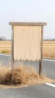 A weathered blank wooden sign stands stoically beside a quiet country road, framed by vast, golden fields under an expansive sky, inviting contemplation. photo