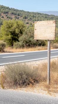 Weathered wooden signpost stands by an empty road, inviting custom text against a backdrop of sun-drenched hills and arid natural landscape. photo