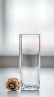 Elegant still life featuring a clear empty glass alongside a beautifully dried rose, bathed in soft, natural light on a minimalist white surface. photo