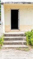 Weathered concrete steps lead to an open, dark doorway of an old, neglected building, evoking a sense of mystery and forgotten history. photo