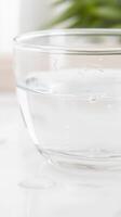 Crisp, Pure Water in a Clear Glass Bowl with Delicate Droplets on a Pristine White Surface photo