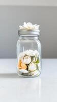 Elegant white and soft orange faux flowers beautifully arranged in a clear glass mason jar, creating a serene and minimalist home decor accent. photo