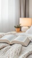 Open book resting on a soft, knitted blanket in a cozy bedroom, illuminated by a warm bedside lamp, perfect for relaxation and quiet reading moments. photo