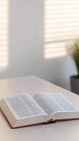 Open Bible on a serene table, illuminated by gentle window light and shadows. Ideal for quiet spiritual study, faith, and peaceful reflection. photo