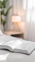Open Holy Bible resting on a pristine white bed, bathed in soft morning light. A serene scene for spiritual study, quiet reflection, and peaceful devotion. photo