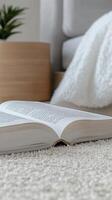 An open book rests on a plush white carpet, inviting quiet moments of reading and reflection in a serene, minimalist home environment. Perfect for leisure and learning. photo