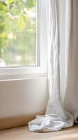Bright natural light streams through a modern window, illuminating a soft white linen curtain cascading onto a warm wooden floor, creating a serene and inviting domestic interior space. photo