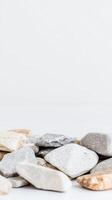 A serene composition of natural river stones and pebbles, showcasing their varied textures and earthy tones against a pristine white background, ideal for calming design. photo