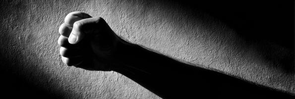 Clenched Fist Silhouette Casting a Long, Harsh Shadow on a Textured Wall During Dim Lighting photo