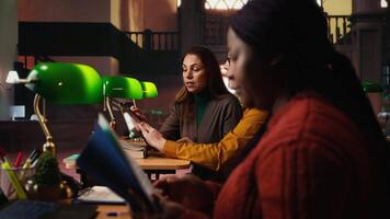 African american woman asking people to keep quiet in the library, struggling to read a book due to noise and disrespect. Making a polite request for the library etiquette. Camera A. video