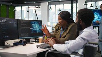 Cheerful manager and employee with paraplegia in inclusive workplace developing software applications. African american technician and colleague with disability using AI to solve bottlenecks, camera A video