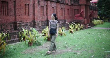 Young woman wearing a striped shirt and green pants walking around, admiring the natural scenery and ancient brick structures, Enjoy holiday travel. video
