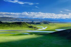 Serene Green Grassland Landscape with River and Distant Mountains under Sunny Sky photo