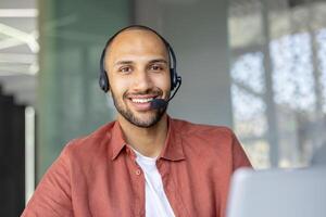 Smiling man wearing a headset, possibly a customer service representative, looking directly at the camera with a welcoming expression. photo