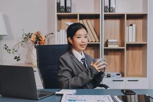 Asian business woman sitting at desk with laptop and coffee photo