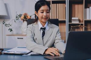 A young asian woman in a business suit sitting at a desk with a laptop photo